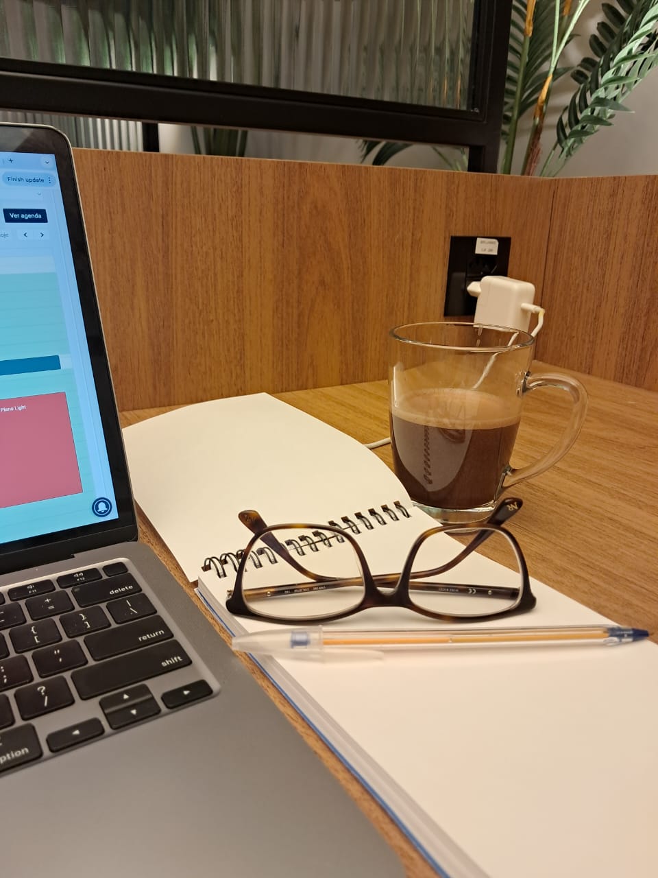 Mesa de trabalho com laptop, óculos, caderno e xícara de café